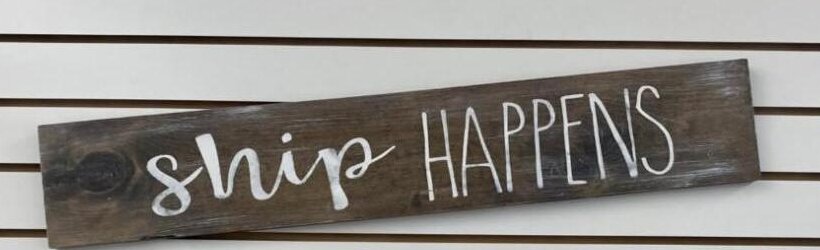 A wooden sign at ShipPro that reads ship happens